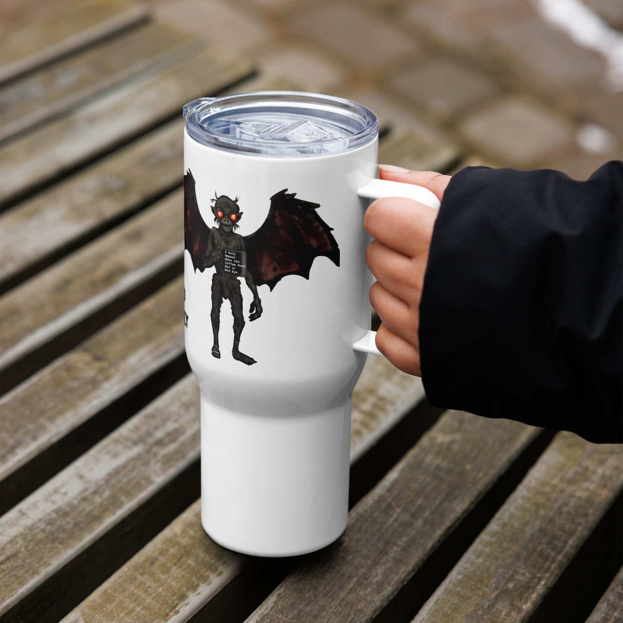 Too Early travel mug held in hand on outdoor bench, showing Mothman with red eyes and "Too Early" text on white stainless steel mug - 25 oz