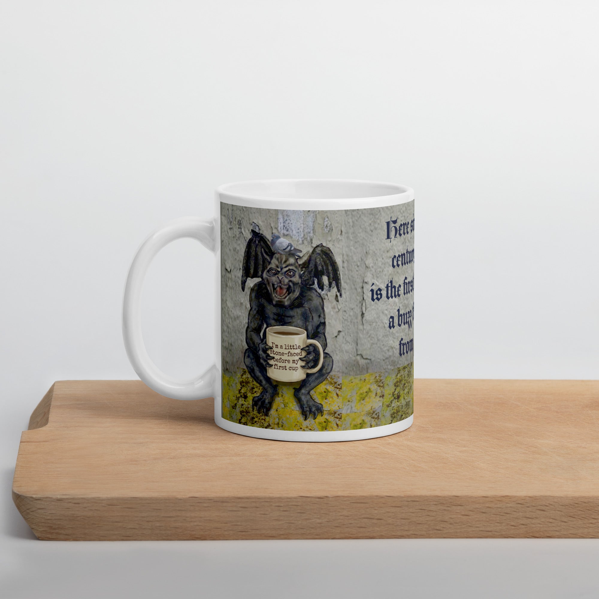 Premium white ceramic Gargoyle mug- Grumpy gargoyle with bat wings and  pigeon on his head holding a coffee mug with "I'm a little stone faced before my first cup" written on it. 11 oz left view