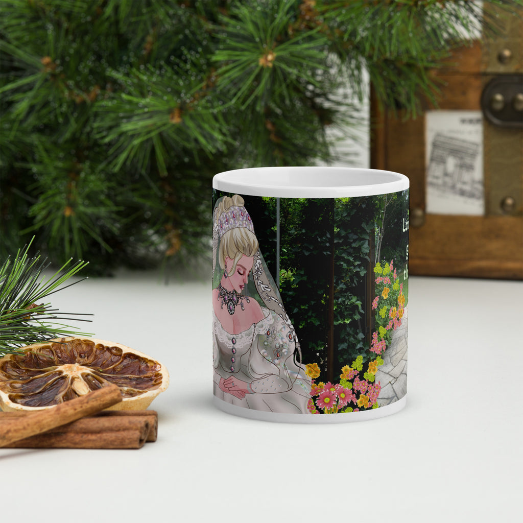 Mug with a decorative design featuring a bride and flowers, placed on a surface with greenery and cinnamon sticks.