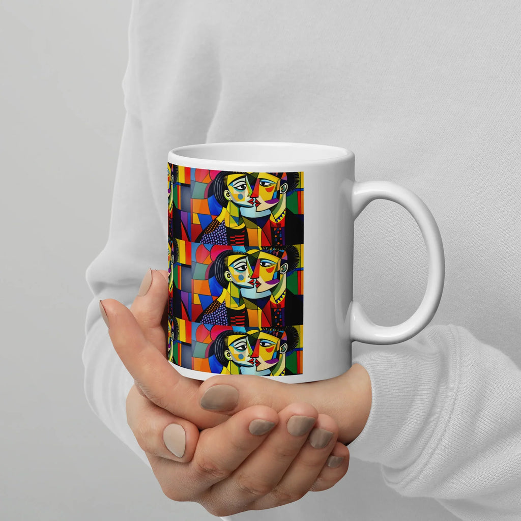 White ceramic mug with colorful abstract face art, held in hands, on white background.