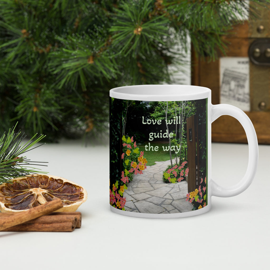 Mug with garden scene and quote 'Love will guide the way' on a table with decorative items.