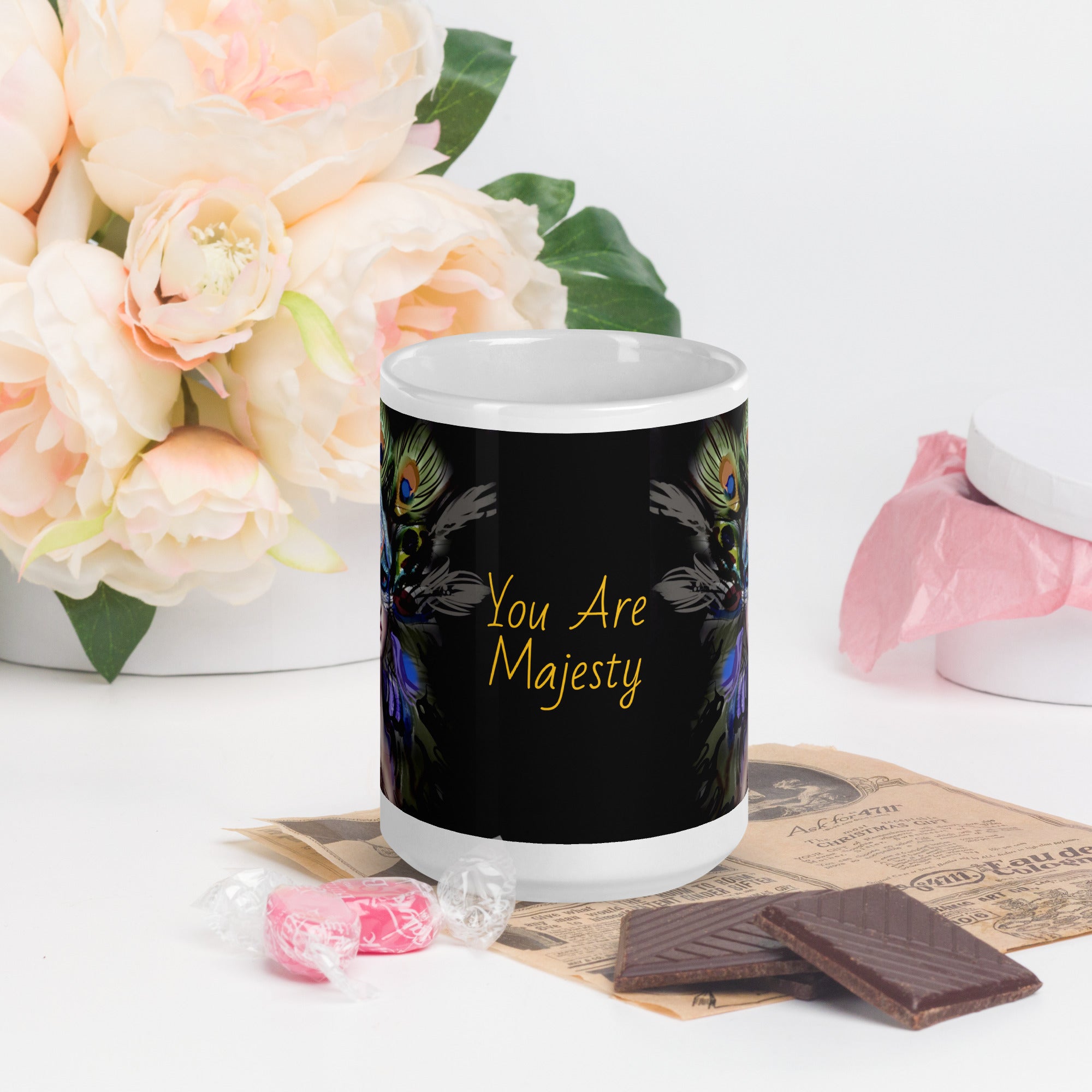 Stunning Premium white ceramic mug features a majestic woman adorned with vibrant peacock feathers, ornate blue and orange face paint, and a regal purple and green costume. With the inspiring message "You Are Majesty, 15- oz front view