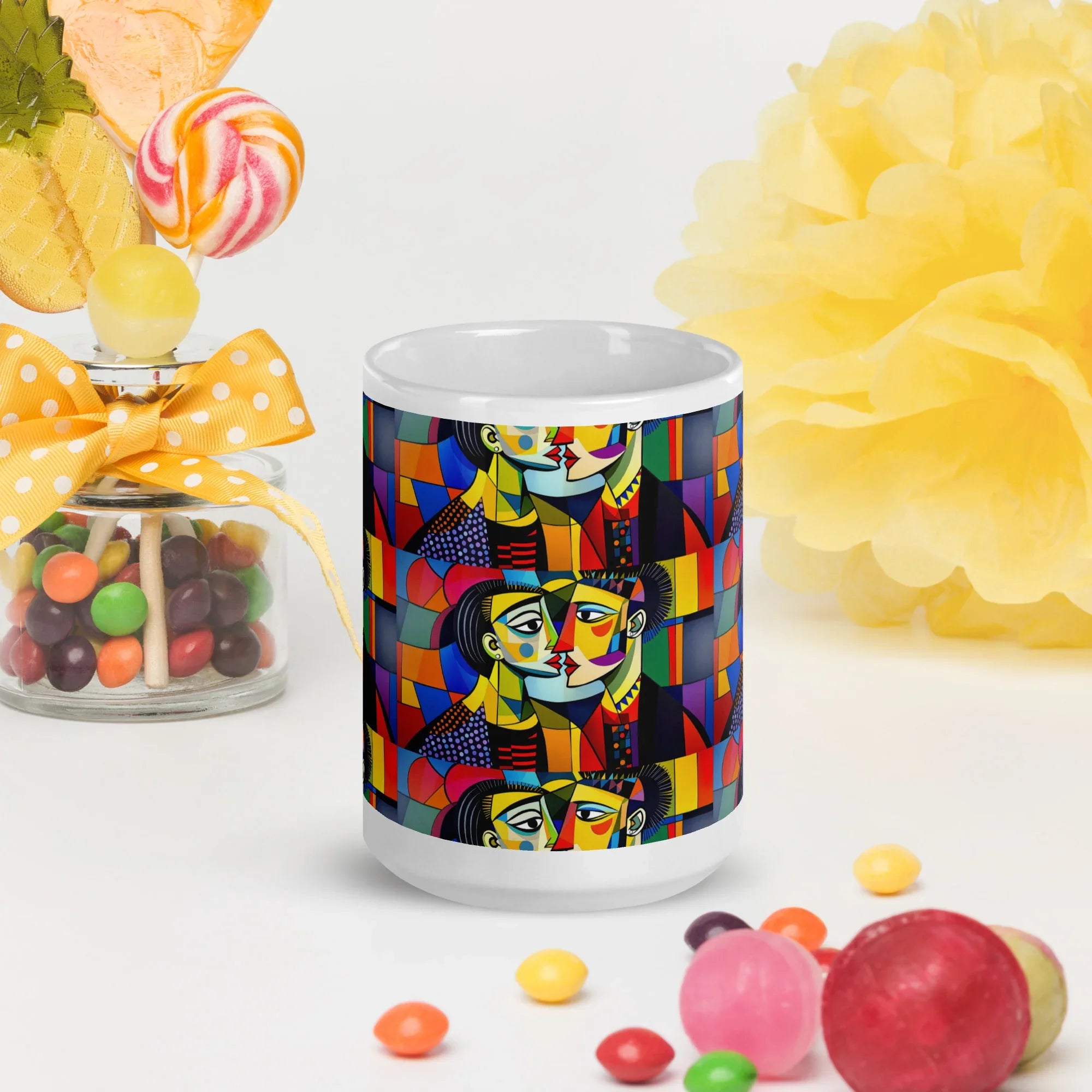 White ceramic mug with colorful abstract face design, surrounded by candies and yellow decor