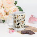 White ceramic mug with colorful cat and butterfly design, flowers and chocolates nearby