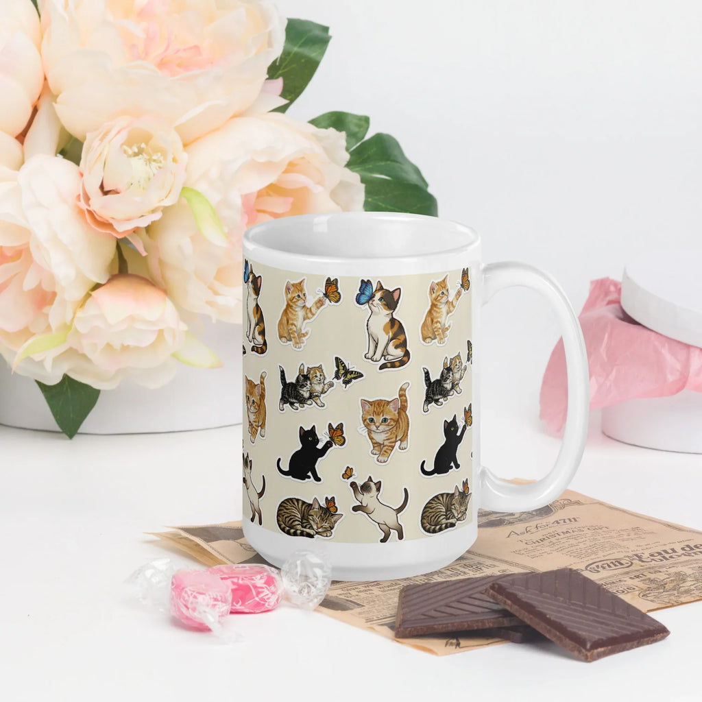 White ceramic mug with playful cat and butterfly illustrations, on table with flowers and chocolate