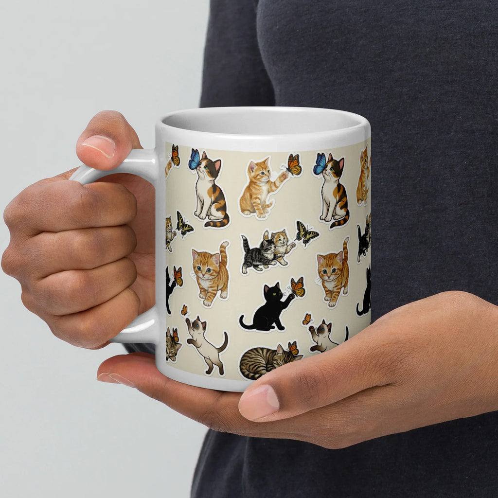 White ceramic mug with playful cat and butterfly illustrations, held in hand.
