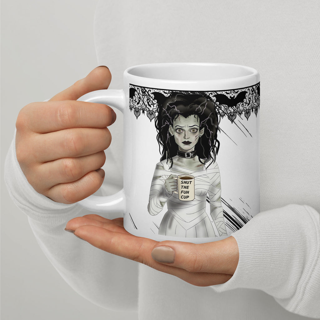 Shut the Fuh Cup Mug - Bride of Frankenstein Coffee Gothic | Brew Crew- Premium white ceramic mug -Frankenstein's monsters bride wearing a white dress made of bandages, and a black choker - her hair is disheveled  and with her blank stare she holds her coffee mug with text "shut the fuh cup" written. Gothic bat lace on top rim - 20 oz- left view