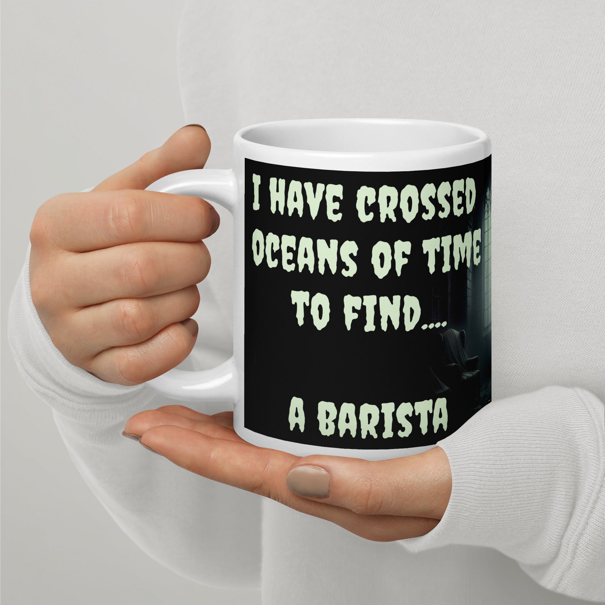 Dracula Coffee Mug - I Have Crossed Oceans of Time to Find a Barista- Premium white ceramic mug with text "I HAVE CROSSED OCEANS OF TIME TO FIND... A BARISTA" - Black background - creepster font in pale green shade.  mug held in persons hand -20 oz left view