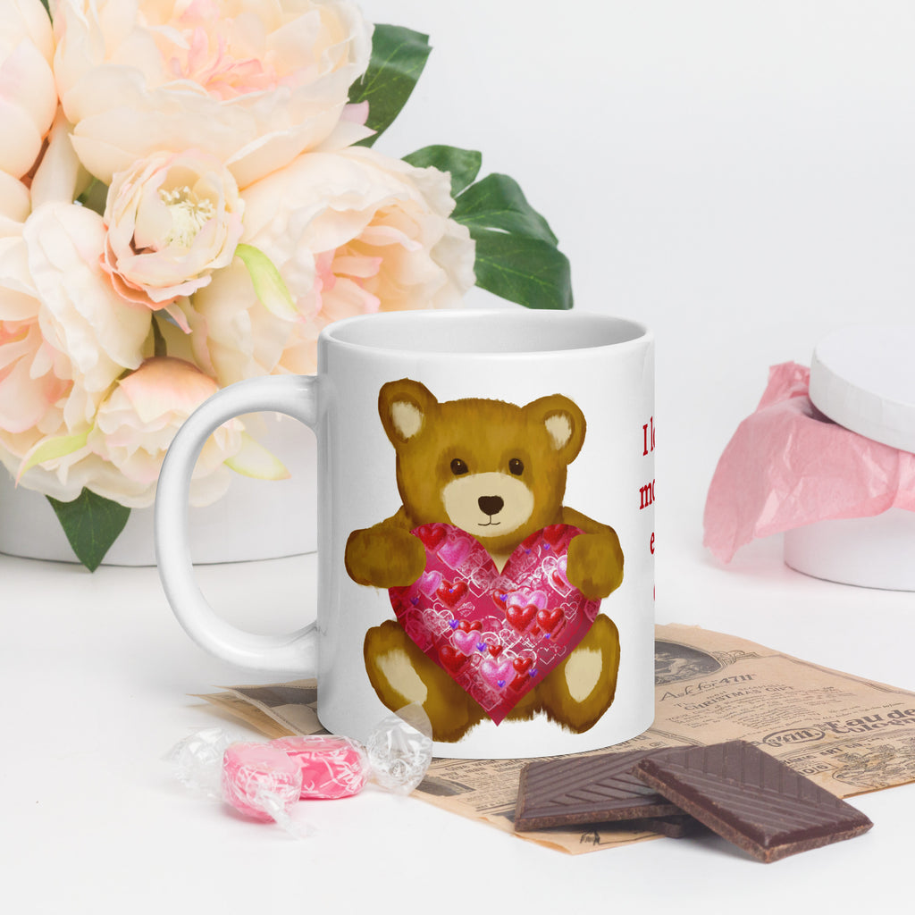 Premium White Ceramic mug - held in persons hand on a table with flowers, a newspaper and chocolate - Valentines Day Bear with geometric Pink and red heart coffee mug. 20 oz - left view